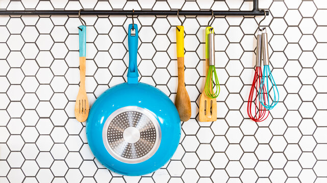 Kitchen pans and spoons hanging on a metal wall rack against hexagon tile wall. Kitchen tools stylish background