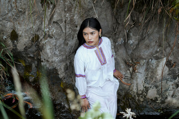 Indigenous woman wearing traditional clothes posing by a rocky river