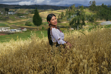 Indigenous woman wearing traditional clothes posing in a field of wheat with andean landscape in the background