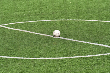 A soccer ball rests on the center line of a synthetic green football field, poised for the start of a game