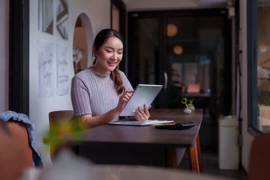 Asian adult freelancer uses tablet working at modern coworking space digital nomad productivity remote office cafe environment