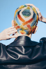 woman with colorful geometric shaved hairstyle wearing black leather jacket stands against clear...