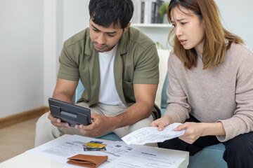 Stressed and headache asian couple with large bills or invoices no money to pay to expenses and...