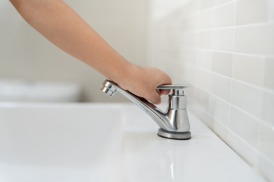 Little kid hand closed the faucet at sink in house with mom. Mother teaches child to save water. keeps turning off the water to save world energy and protect the environment, world water day - Powered by Adobe