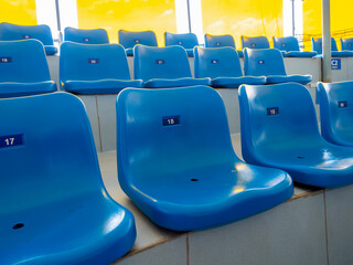 Scene of seat numbers on empty blue plastic chairs, in stadium or aquarium show. Rows of seats...