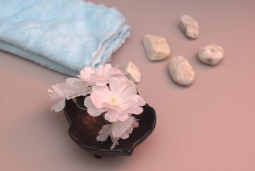 Minimalist arrangement of a red tealight candle, white decorative flowers, and a rolled blue towel. Warm and calming tones, perfect for use in spa, self-care, or relaxation-themed visual content.