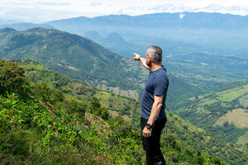 Outdoor portrait of a serious and confident adult man standing on a green mountain with a beautiful landscape view during a travel adventure in the Colombian Andes, South America.
