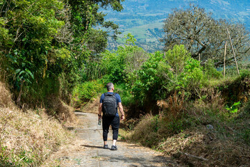 Male hiker with a backpack seen from behind, standing on a mountain summit and looking at the spectacular view of the green valley and landscape during an adventure travel trip in the Andes, Colombia.
