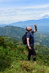 Exhausted male hiker drinking water during a hot summer day hiking in the beautiful green mountains...