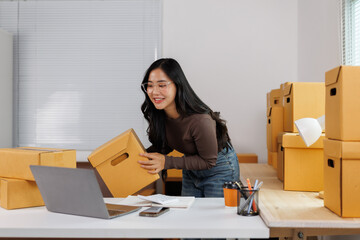 Online seller preparing cardboard box for delivery using laptop