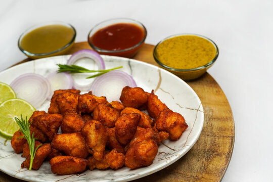 Chicken or fish pakoda or pakora platter ,three different flavours of sauce ,pakora arranged in a white plate and garnished with onion and lemon silce on a wooden background.