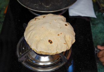 Close up shot of cooking a roti or chappati being roasted puffed and swollen on a blue gas flame in the kitchen