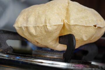 Close up shot of cooking a roti or chappati being roasted puffed and swollen on a blue gas flame in...