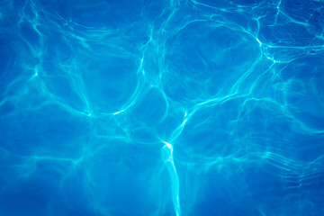 Clear blue swimming pool water surface with sunlight reflections creating abstract patterns and ripples, evoking a refreshing and tranquil summer vibe.
