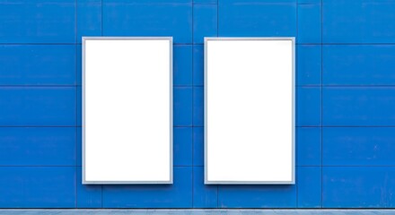 Two blank white posters in silver frames are mounted on a blue tiled wall