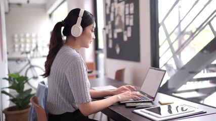 Young Asian woman remote working from modern cafe using laptop headphones for online business global freelancer digital nomad lifestyle productivity - Powered by Adobe