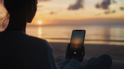 Silhouette of person viewing sunset on a beach through a mobile phone.