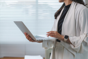 Businesswoman working on laptop in modern office, holding and typing