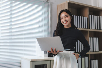 Portrait of smiling businesswoman holding laptop in office