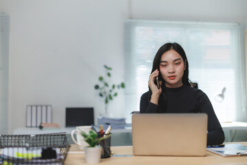 Focused asian businesswoman making a business call and working on a laptop in office