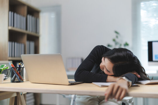 Exhausted asian office worker sleeping at desk after working late