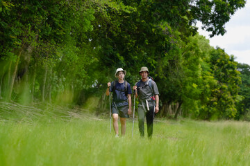 Fototapeta premium Happy tourist hiking walking together over grassland of the plains. Active young adult man trekking through nature grass field over lowland in rural trail. Portrait of real people in peaceful meadow.