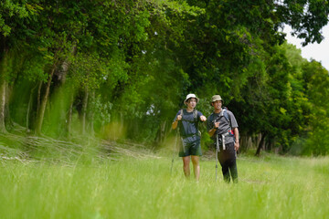Obraz premium Happy tourist hiking walking together over grassland of the plains. Active young adult man trekking through nature grass field over lowland in rural trail. Portrait of real people in peaceful meadow.