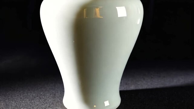 Elegant white vase casting soft shadows on a dark surface, highlighting its smooth curves