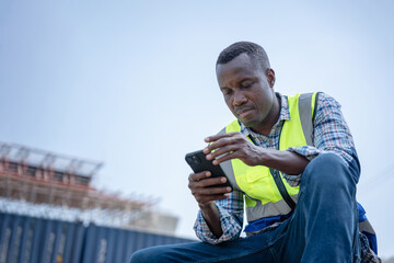 Construction Worker Using Smartphone on Job Site, Engineer in Safety Vest Checking Phone at Work,...