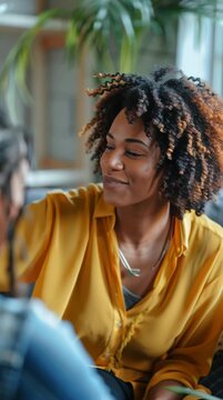 Smiling young adult woman with curly hair and medium skin engages in conversation indoors