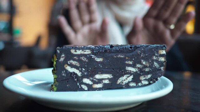 slice of cake on a plate with a person saying no to sweet in background,