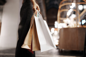 Stylish young woman walking outdoors at night, carrying shopping bags with joy, surrounded by city...