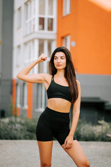 Woman posing confidently in activewear against a modern orange building backdrop