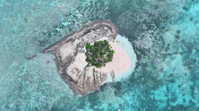 Top-down drone spin showing Guyam Island in Siargao, Philippines, a tiny islet with palm trees, white beach, and coral reef surrounded by shallow turquoise water in the tropical Pacific Ocean.