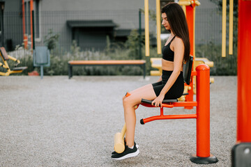 Woman exercises with outdoor fitness equipment at a park during daylight hours