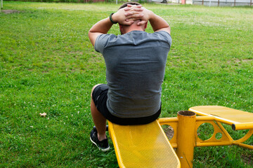 Man doing sit-ups outdoors on yellow exercise equipment. Workout in a park setting.