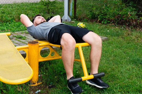 Man doing sit-ups on outdoor fitness equipment in a park. - Powered by Adobe