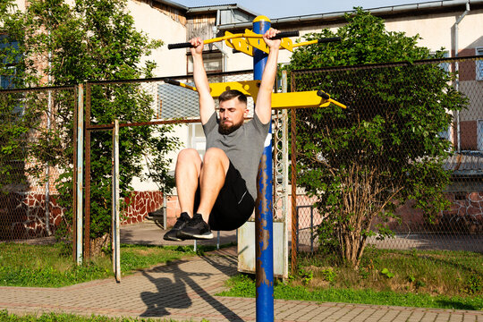Man doing hanging leg raises outdoors on a sunny day. Great for core strength and fitness.