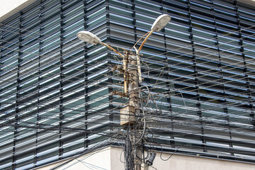 Power pole with electric lamps and cables in front of a modern office building facade, photo taken in Romania.