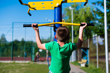 Boy doing pull-ups on outdoor fitness equipment. Healthy lifestyle and outdoor exercise.