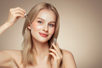 Young beautiful blonde woman applying face serum with pipette. Cosmetic procedures for facial skin...