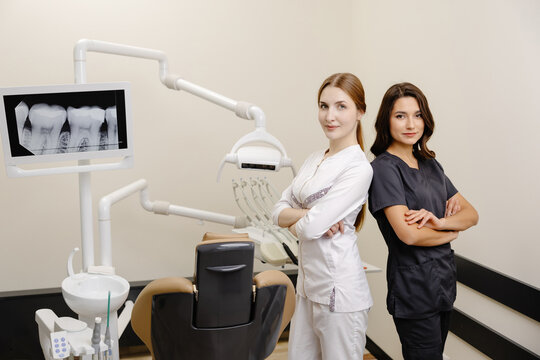 Smiling dentist and assistant with crossed hands looking at the camera in dental clinic