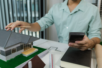 Asian male architect working with a calculator at his desk in a modern office. Surrounded by house...