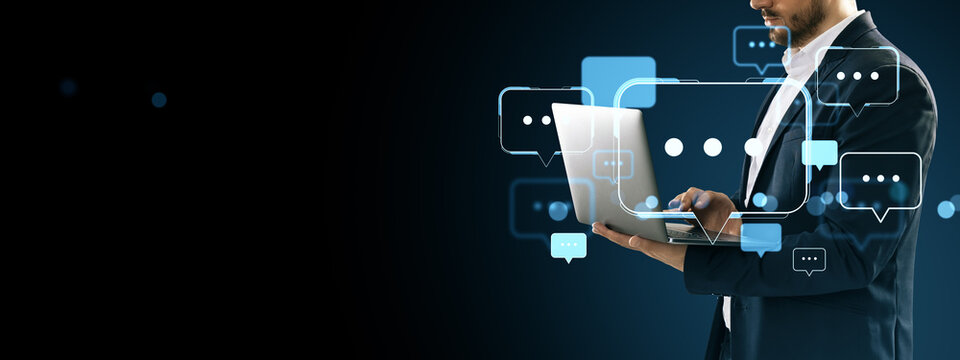 Businessman using laptop surrounded by digital speech bubbles on dark tech background, representing online communication and innovation.