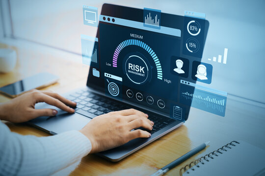Business person analyzing digital risk management interface on laptop at desk with futuristic financial data dashboard and corporate charts.