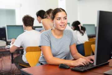 Cheerful woman sitting at desk in computer class and using PC, learning to use software.