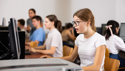 Clever female teenager wearing glasses and solving tasks of computer science in the auditory