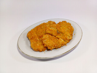 Pieces of golden-brown, crispy breaded chicken cutlets, presented on a white oval plate againts a white background, emphasizing the food. Related to fried chicken, breaded cutlets, Japanese cuisine