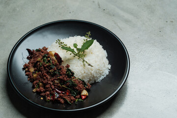 home made Thai's style spicy stir fried basil with minced beef served with Thai jasmine rice in black dish put on naked gray concrete texture 
dinner table with small free copy space on a side