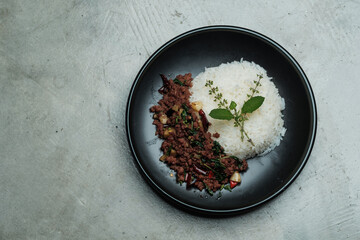 home made Thai's style spicy stir fried basil with minced beef served with Thai jasmine rice in black dish put on naked gray concrete texture 
dinner table with small free copy space on a side